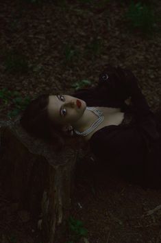 a woman laying on top of a tree stump in the woods with her eyes closed