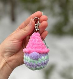 a hand holding a small crocheted keychain with a pink and purple cone on it