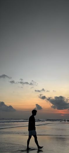 a man walking on the beach at sunset with his foot in the water and clouds above him