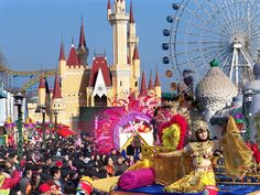 a parade float in front of a castle and ferris wheel with lots of people around it