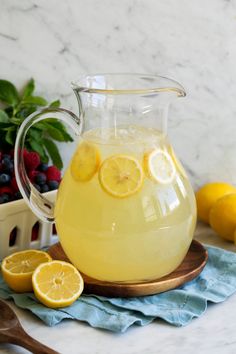 a pitcher filled with lemonade sitting on top of a table next to sliced fruit