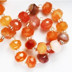 an orange and red beaded necklace on a white surface with other beads in the background