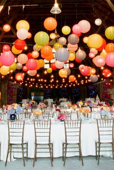 the tables are set up with paper lanterns hanging from the rafters over them for an elegant reception