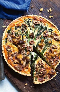 a quiche with asparagus and other toppings on a cutting board next to a knife