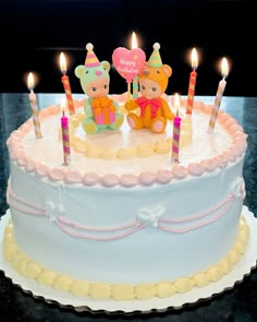 two teddy bears sitting on top of a birthday cake with candles in the shape of hearts