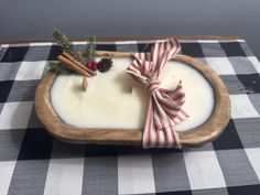 a wooden tray holding a candle and some cinnamon sticks on top of a checkered table cloth