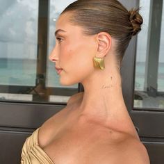 a woman with large gold earrings on her neck looking out the window at the ocean