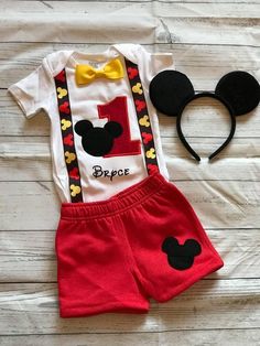 a mickey mouse outfit and headband on a white wooden background with a yellow bow