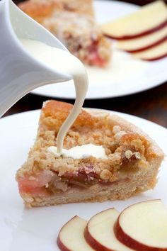 a piece of pie on a plate with apples and cream being drizzled over it