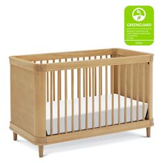 a wooden crib with white sheets in front of a greenguard sticker on the wall