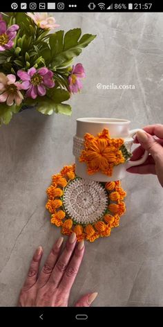 two hands are reaching for an orange flower on top of a white cup and saucer