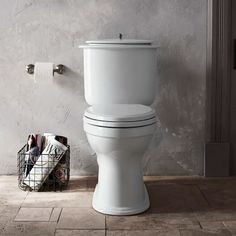 a white toilet sitting on top of a bathroom floor next to a basket with towels