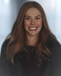 a woman with long brown hair smiling at the camera and wearing a black blazer