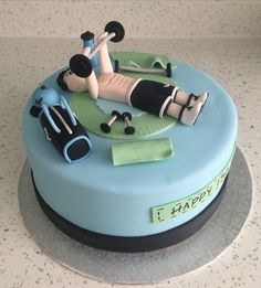 a birthday cake with a woman laying on the ground and some exercise equipment around it