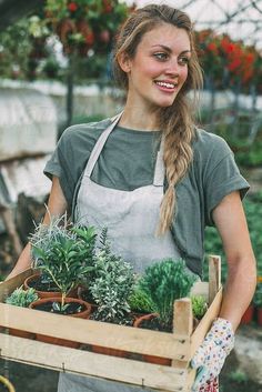 a woman holding a wooden crate filled with plants