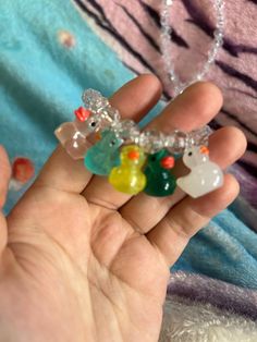 a hand holding a small multicolored bear and heart charm necklace on it's palm