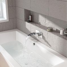 a white bath tub sitting under a window next to a sink with faucet