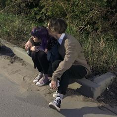 two people sitting on a cement bench with their faces close to each other and one is kissing the other