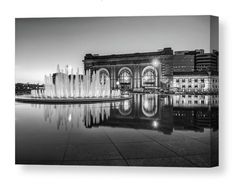 a black and white photo of a fountain in front of a building with lights on it