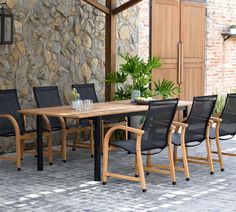 an outdoor dining table with four chairs and a potted plant in front of a stone wall