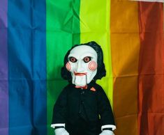 a creepy doll sitting in front of a rainbow flag