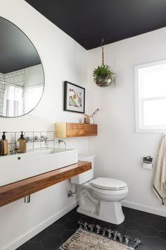 a white toilet sitting under a bathroom mirror next to a sink in a room with black tile flooring