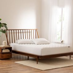 a bed sitting on top of a hard wood floor next to a white curtained window