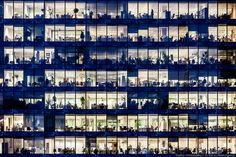 an office building is lit up at night with many windows and people working in it