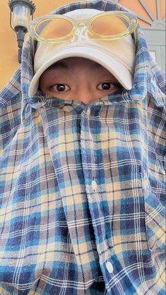 a person wearing a blue and white plaid jacket with glasses on their head, covering his face