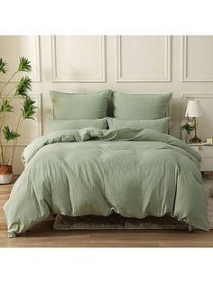 a bed with green sheets and pillows in a room next to a potted plant