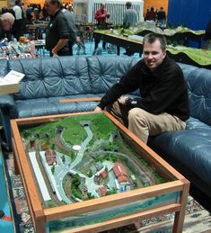 a man sitting on a blue couch in front of a table with a model train