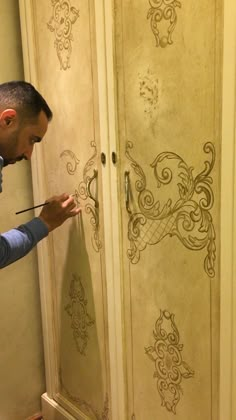 a man painting the side of a closet with decorative designs on it's doors