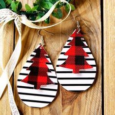 pair of red and black plaid christmas tree earrings on wooden table next to greenery