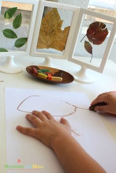 a child's hand is drawing on paper with colored crayons and leaves