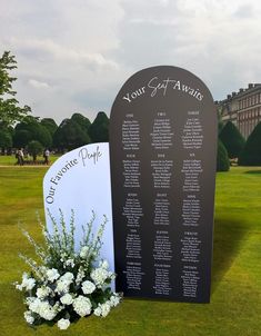 a black and white wedding seating chart with flowers in front of it on the grass