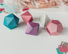 several different colored origami pieces on a white surface with christmas lights in the background