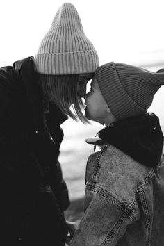 black and white photograph of a woman kissing a small child's nose with water in the background