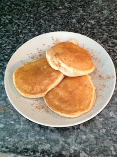 three pancakes on a white plate sitting on a granite counter top with cinnamon sprinkles