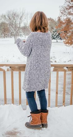 a woman standing on top of snow covered ground next to a wooden fence with trees in the background