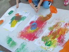 two children are painting on paper with orange and green colors