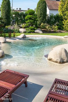 two wooden benches sitting in front of a small pool with rocks and water running through it