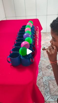 a young boy is sitting at a table with cups and beads in front of him