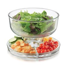 a glass bowl filled with salad next to another bowl full of tomatoes, cucumbers and croutons