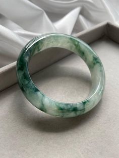 Item Code: JBG223013 Grade 'A' Burmese Jadeite Bangle The marbling in this jade bangle is blueish green which is very rare. The coarse texture of this bangle has created an added value for its green marble surrounding it, making it seems like the marbling is still spreading across the bangle. The crystalline structure inside the bangle is strong yet compliments to green marble creating a moving illusion. Though it may seem the texture is coarse but upon closer look, the jade bangle has reached a jelly like surface which signifies an aged jade beneath the earth.  The bangle has some veins at the inner corners of the bangle but it does not affects the quality of the bangle.  Measurements: Size: 57.2mm Width: 14.6mm Thickness: 8.2mm This piece will be sent to our local Singapore Gem Laborator Pinterest Jewelry, Floating Flowers, Jewelry Photoshoot, Jade Bangle, Baby Oil, Jade Jewelry, Classy Jewelry, Jade Beads, Jewelry Inspo