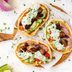 three pita breads filled with meat, vegetables and cucumbers on a cutting board