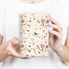 a woman holding a notebook in her hands with flowers all over it and writing on the cover