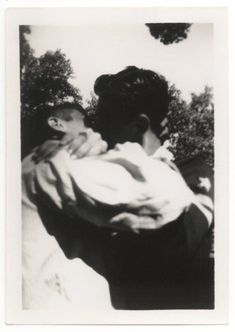 an old black and white photo of a man holding a child in his arms with trees in the background