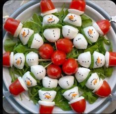 a white plate topped with tomato and mozzarella snowmen on top of lettuce