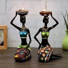 two african women holding trays on their heads sitting on a table next to a potted plant