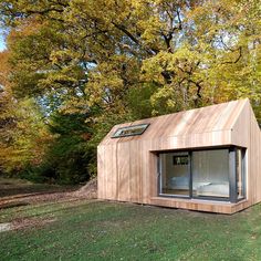 a small wooden building sitting in the middle of a lush green field next to trees